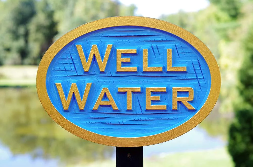 A blue and gold well water sign in front of a pond.