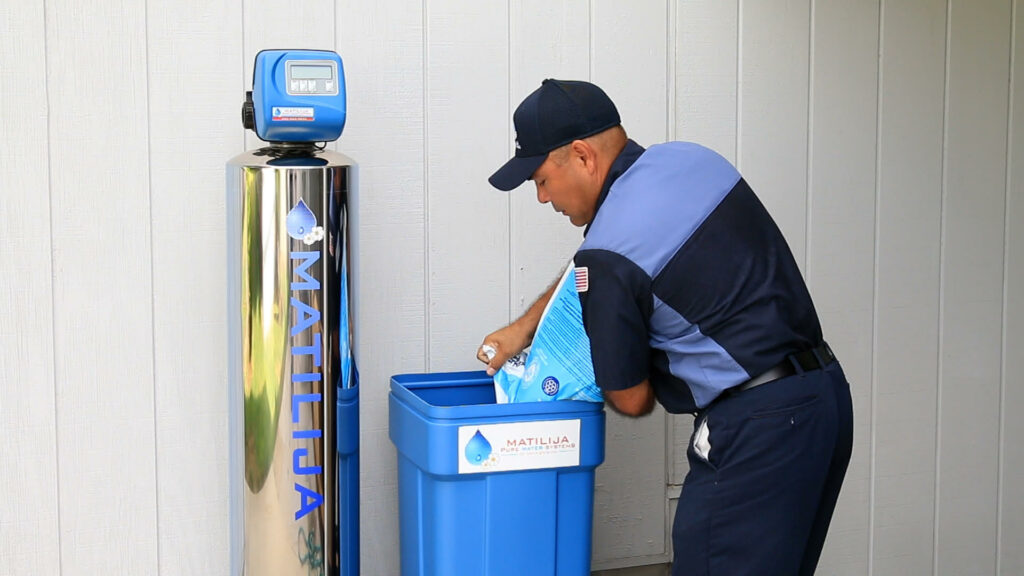 A man is putting a water softener into a trash can.