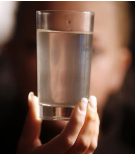 A person holding a clear glass of water in front of their face.